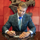 A T-Rex skull mounted against a red wall has its mouth agape behind Vince McMahon who sits at a marble table with a dollar bill in front of him that he is marking with a sharpie as he looks up towards the camera.